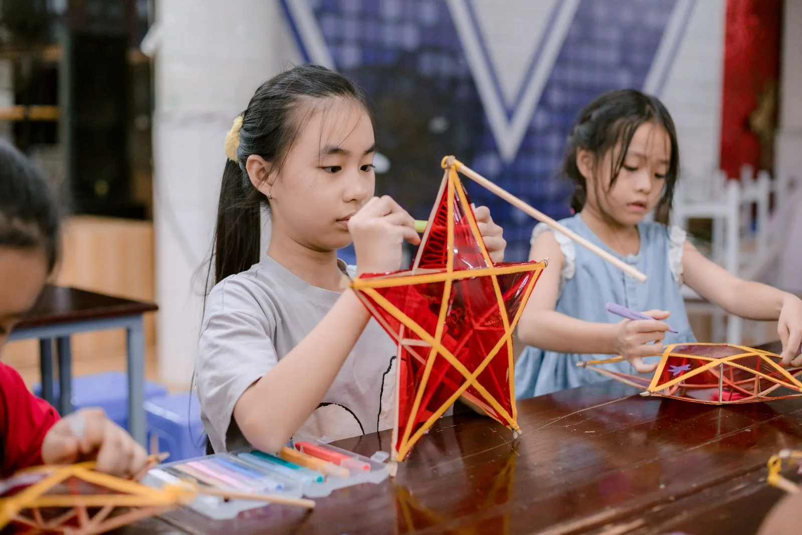 Young girls crafting traditional star-shaped lanterns at a table, engaging in a cultural activity.